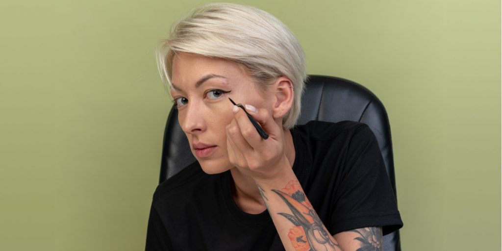 woman with tattoo applying eyeliner