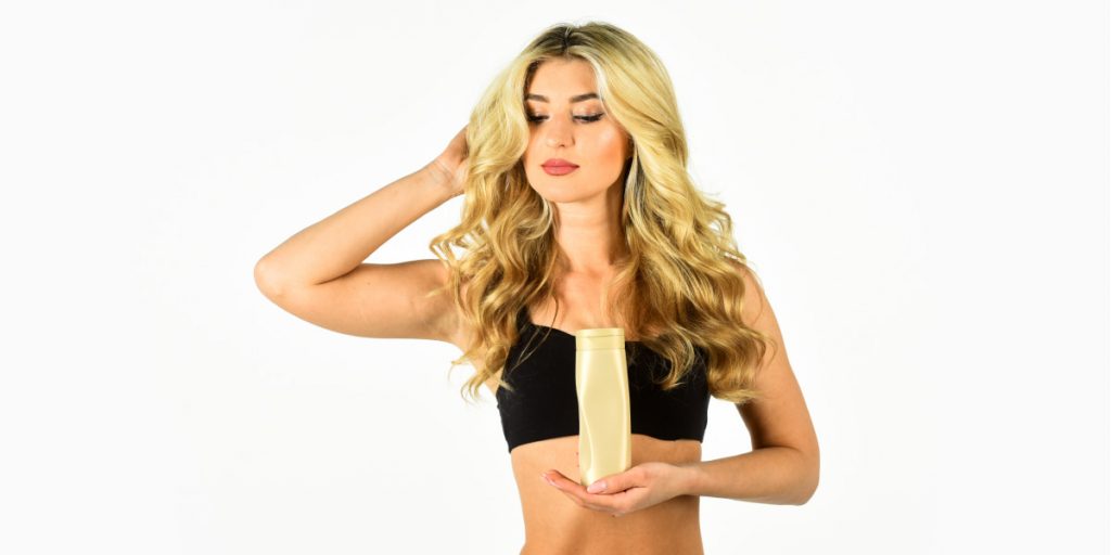 blonde holding shampoo bottle on white background