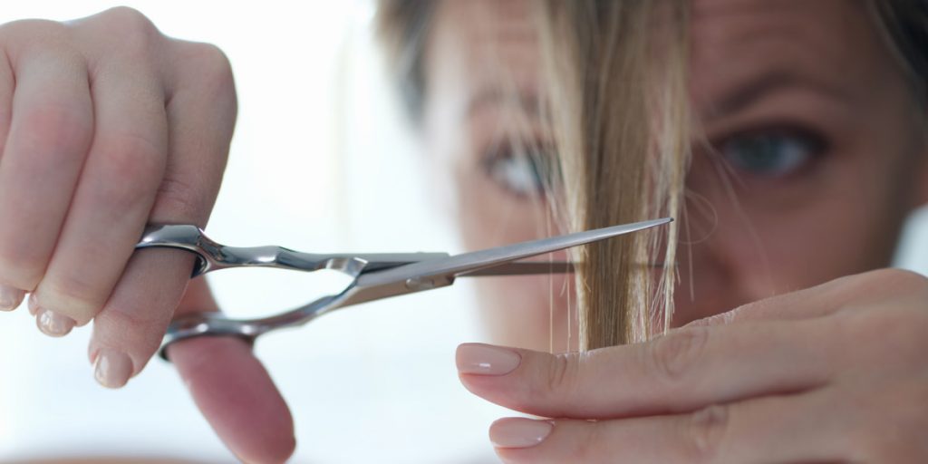 woman is cutting her bang with scissors closeup