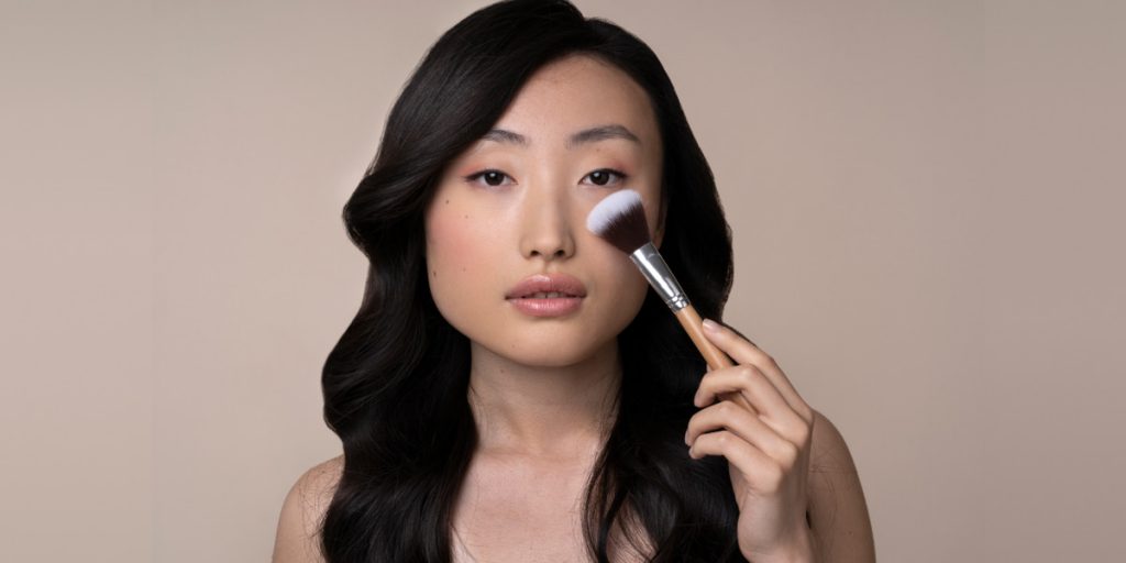 asian girl is applying makeup with makeup brush