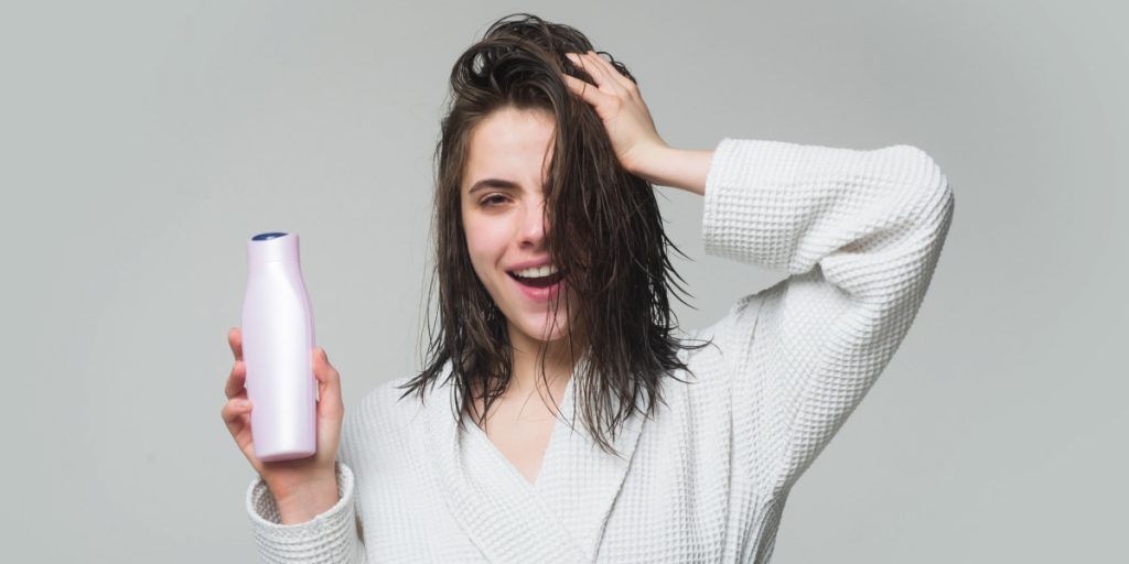 girl with wet hair is holding shampoo bottle