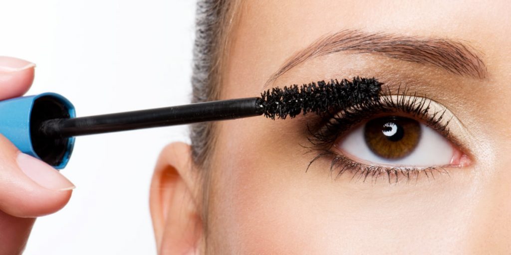 woman with brown eyes applies a mascara